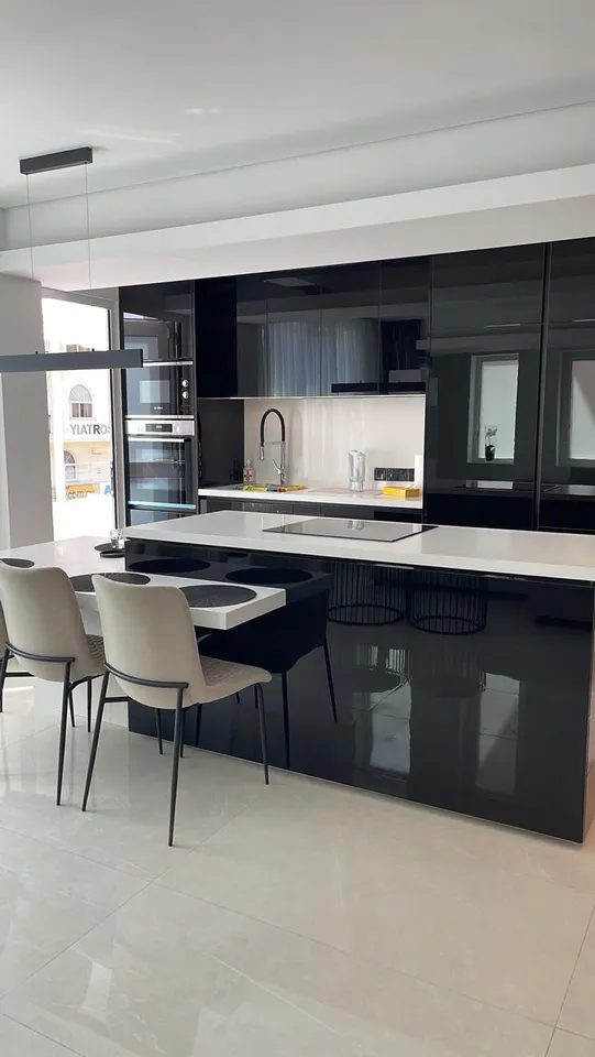 Black gloss kitchen with a white island and pale chairs