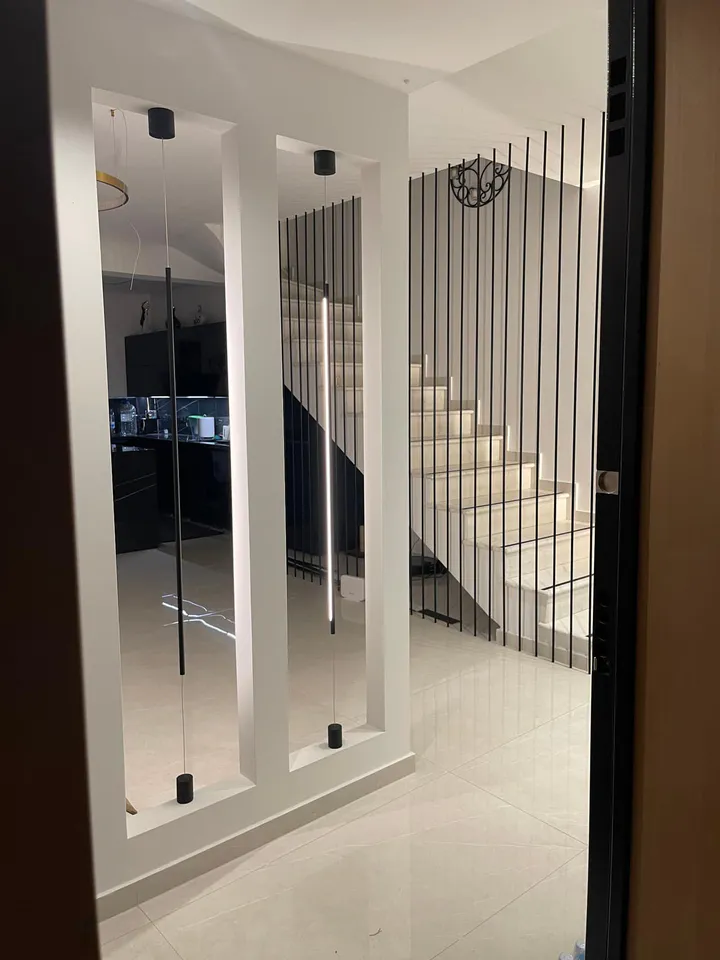 Hallway with lit niches and a staircase behind black vertical rods